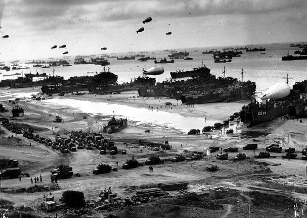 An aerial photograph of the Allied invasion of Europe. The photo shows tanks, blimps, ships, and soldiers arriving on the beach.